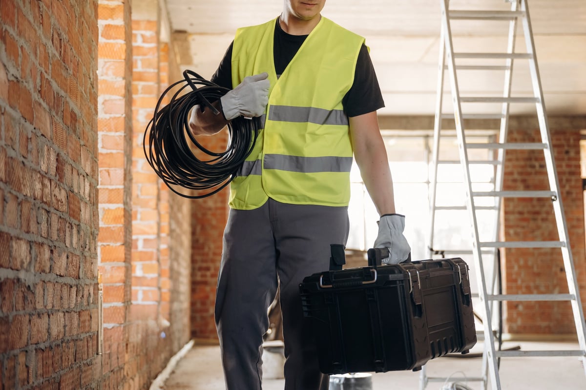 Construction worker carrying a toolbox and cables